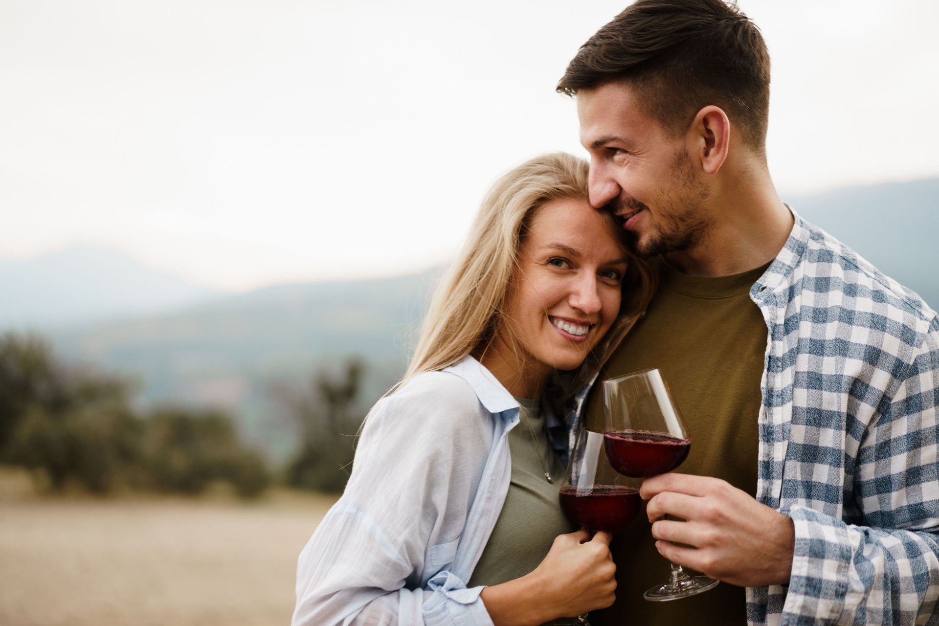 Pareja sonriente brindando por copas de vino al aire libre en las montañas